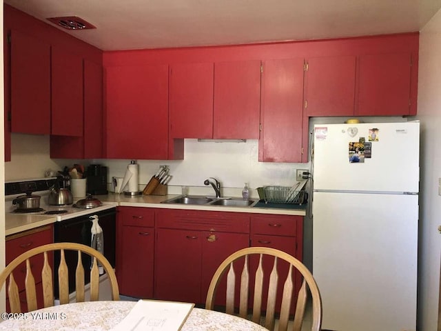 kitchen with freestanding refrigerator, light countertops, range with electric stovetop, and red cabinetry