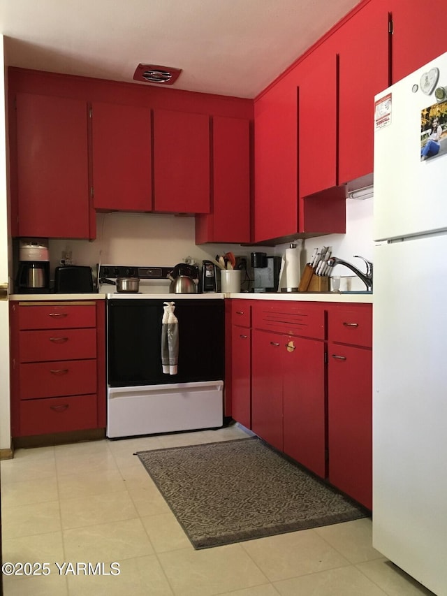 kitchen featuring red cabinetry, freestanding refrigerator, light countertops, and range with electric stovetop