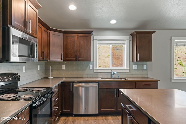 kitchen featuring stainless steel appliances, a sink, wood finished floors, decorative backsplash, and recessed lighting