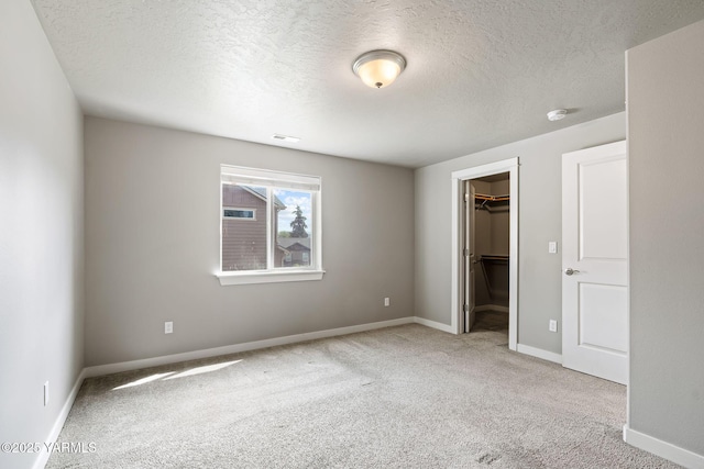 unfurnished bedroom with a spacious closet, carpet flooring, a textured ceiling, baseboards, and a closet