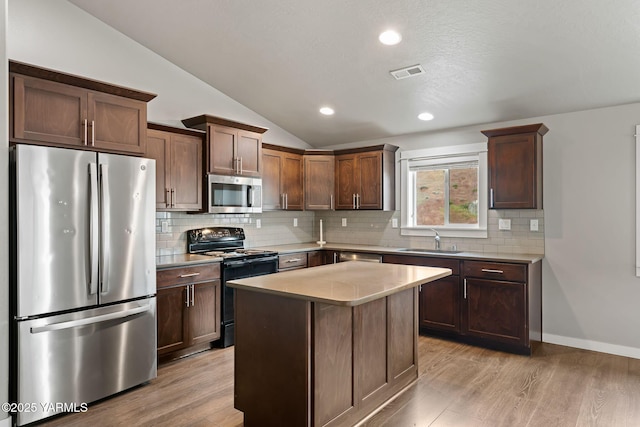 kitchen with appliances with stainless steel finishes, a sink, lofted ceiling, light countertops, and light wood-style floors