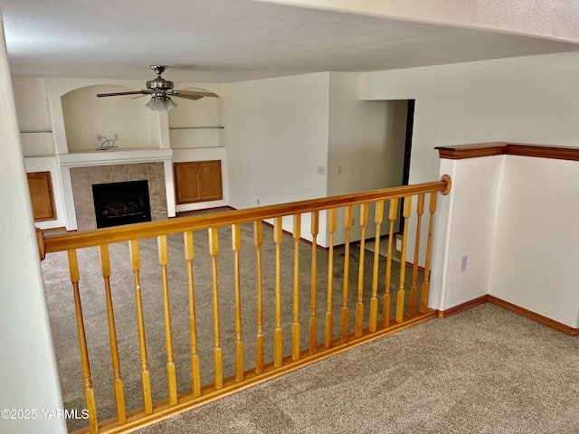 staircase with carpet, ceiling fan, baseboards, and a tile fireplace