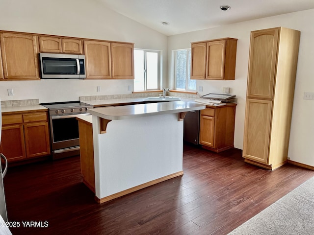 kitchen featuring dark wood finished floors, appliances with stainless steel finishes, a center island, light countertops, and a sink