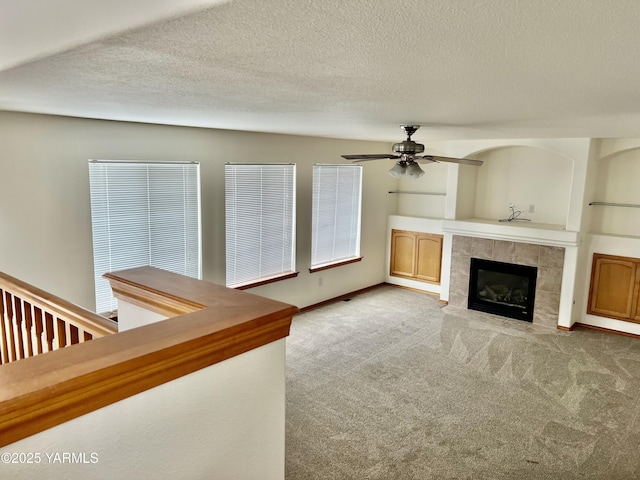 unfurnished living room with a tile fireplace, carpet flooring, ceiling fan, and a textured ceiling