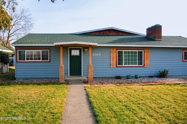 view of front facade with a shingled roof, a chimney, and a front lawn