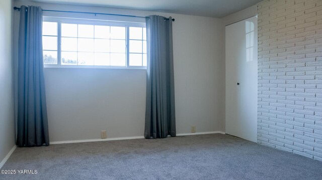 carpeted empty room featuring brick wall