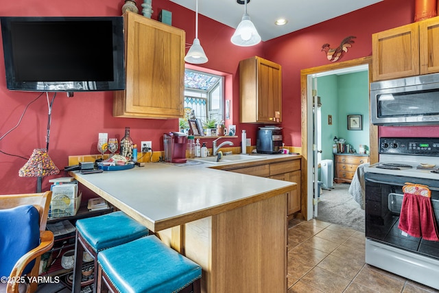 kitchen with a peninsula, a sink, range with electric cooktop, stainless steel microwave, and decorative light fixtures