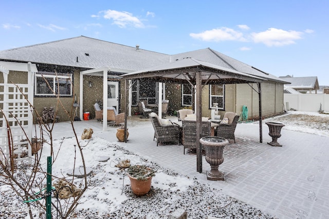 snow covered back of property featuring a shingled roof, fence, and a gazebo