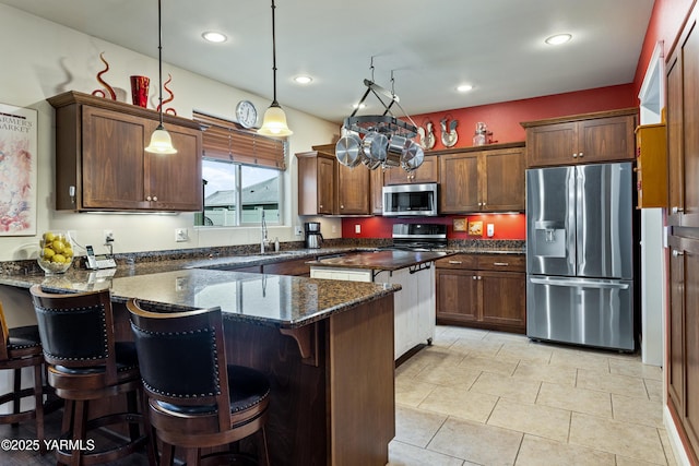 kitchen with pendant lighting, a breakfast bar area, stainless steel appliances, a kitchen island, and dark stone countertops