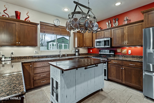 kitchen featuring dark stone counters, appliances with stainless steel finishes, light tile patterned floors, and a sink