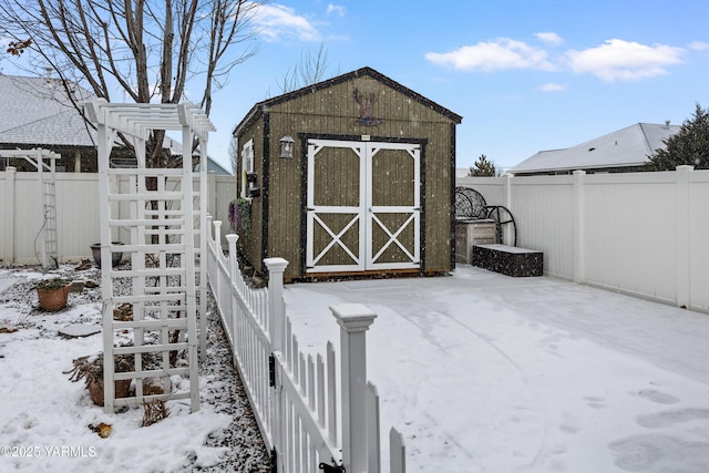 snow covered structure featuring a storage shed, an outbuilding, and a fenced backyard