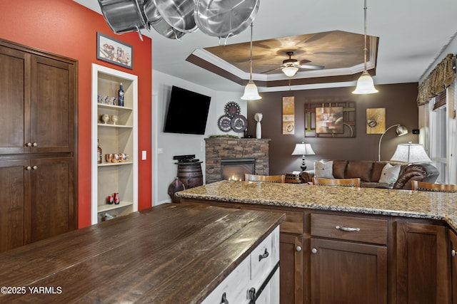 kitchen with open floor plan, dark stone countertops, hanging light fixtures, a tray ceiling, and a fireplace