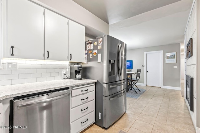 kitchen with tasteful backsplash, white cabinetry, appliances with stainless steel finishes, light tile patterned floors, and baseboards