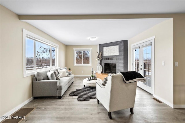 living area featuring a brick fireplace, visible vents, baseboards, and wood finished floors