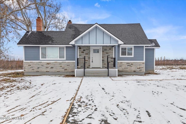 view of front of home featuring stone siding, a shingled roof, a chimney, and board and batten siding