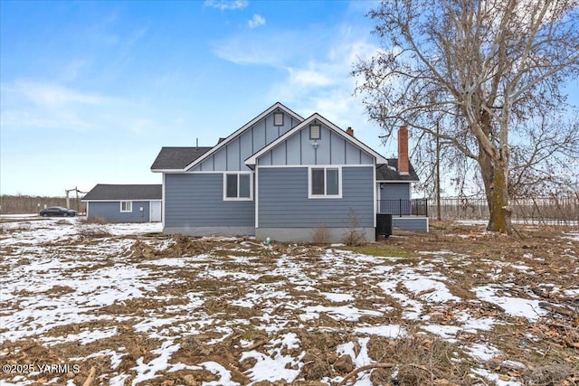 snow covered property with board and batten siding and a chimney