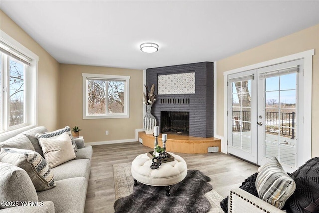 living area featuring light wood-type flooring, french doors, a fireplace, and baseboards