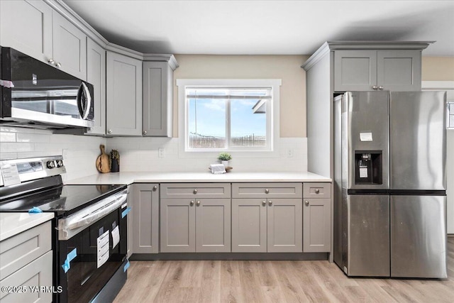 kitchen featuring light countertops, light wood-style flooring, decorative backsplash, gray cabinetry, and appliances with stainless steel finishes