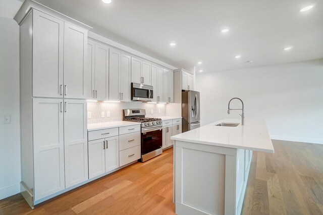 kitchen featuring appliances with stainless steel finishes, backsplash, a kitchen island with sink, and light hardwood / wood-style floors