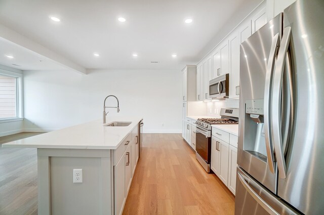 kitchen featuring stainless steel appliances, a kitchen island with sink, sink, white cabinetry, and light hardwood / wood-style floors