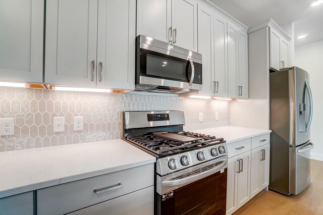 kitchen with light wood-type flooring, appliances with stainless steel finishes, light stone countertops, white cabinets, and decorative backsplash