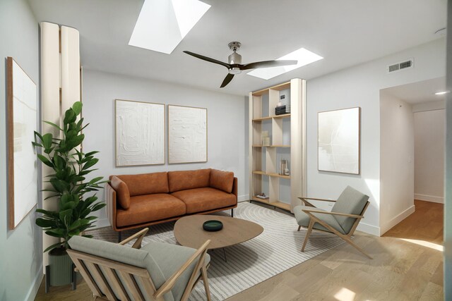 living room with ceiling fan, light wood-type flooring, and a skylight