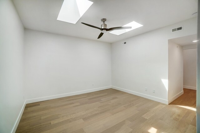 unfurnished room with ceiling fan, a skylight, and light hardwood / wood-style flooring