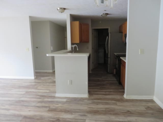 kitchen with a peninsula, light wood finished floors, brown cabinets, and light countertops