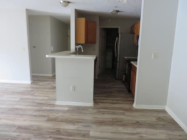 kitchen with a peninsula, light wood-style flooring, brown cabinetry, and light countertops