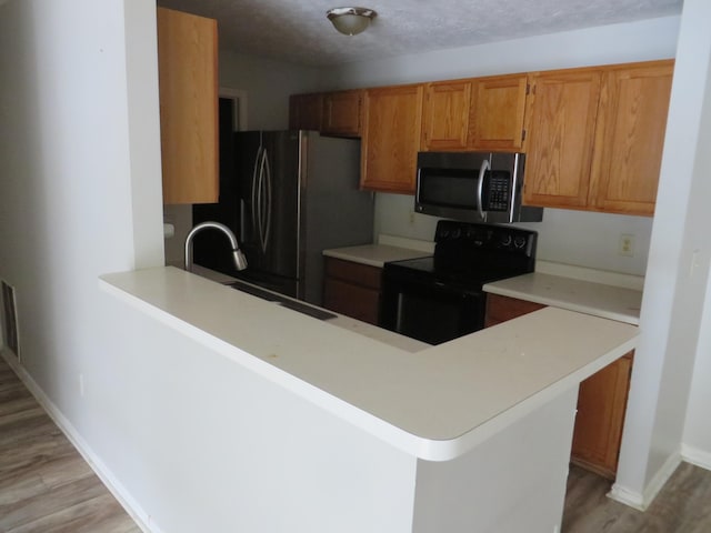 kitchen featuring light countertops, light wood-style flooring, a sink, a peninsula, and black appliances