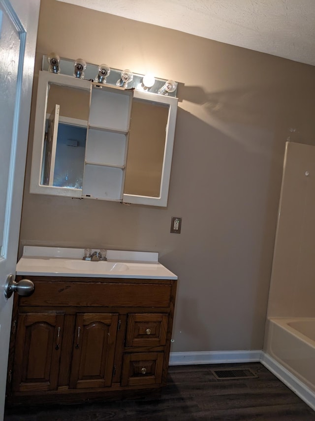 bathroom with hardwood / wood-style floors, a tub, vanity, and a textured ceiling