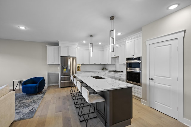 kitchen with appliances with stainless steel finishes, a center island, decorative light fixtures, white cabinetry, and light hardwood / wood-style flooring