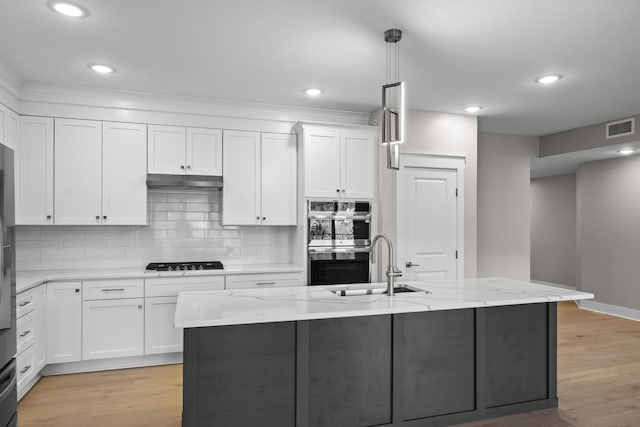 kitchen with light stone countertops, an island with sink, and white cabinetry