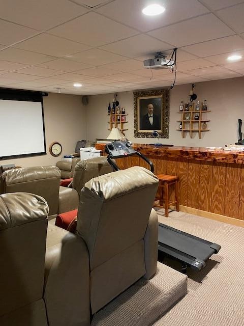 carpeted cinema room with a drop ceiling and bar