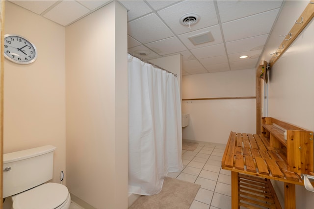 bathroom with tile patterned flooring, a drop ceiling, and toilet