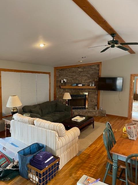 living room featuring light hardwood / wood-style flooring, ceiling fan, a stone fireplace, and beamed ceiling