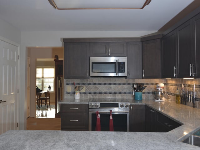 kitchen with light stone countertops, tasteful backsplash, hardwood / wood-style floors, dark brown cabinets, and appliances with stainless steel finishes