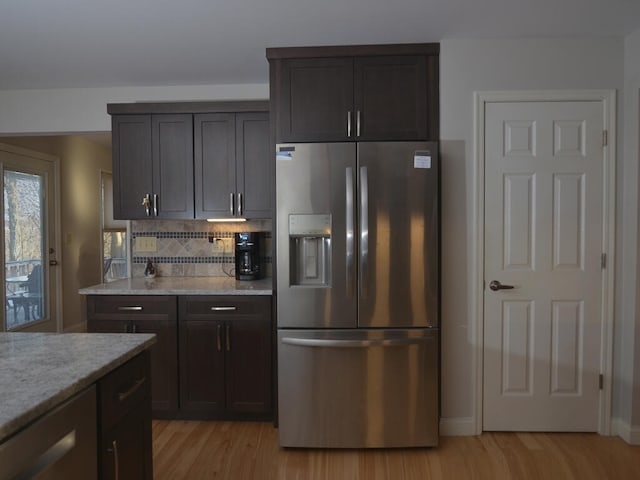 kitchen with stainless steel fridge, light stone counters, dark brown cabinets, light hardwood / wood-style floors, and tasteful backsplash