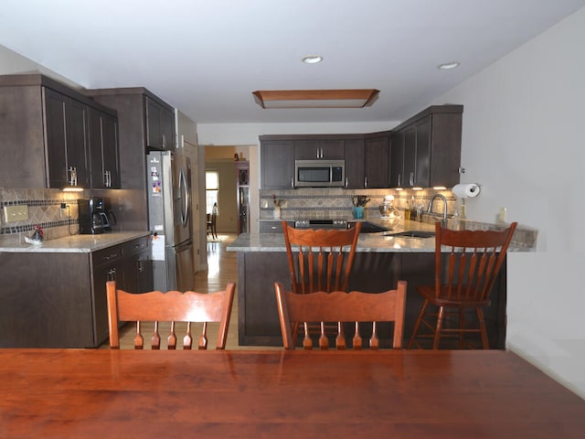 kitchen with kitchen peninsula, sink, light stone counters, appliances with stainless steel finishes, and tasteful backsplash