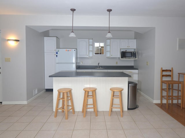 kitchen featuring white fridge, stainless steel microwave, a breakfast bar, light hardwood / wood-style floors, and white cabinetry