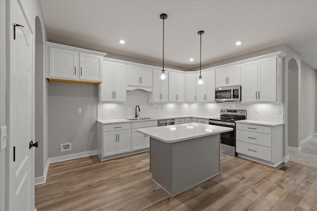 kitchen with sink, white cabinets, appliances with stainless steel finishes, a kitchen island, and light wood-type flooring