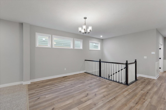 spare room featuring a notable chandelier, light hardwood / wood-style flooring, and a textured ceiling