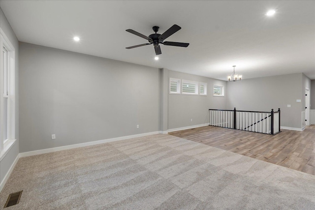 carpeted spare room featuring ceiling fan with notable chandelier