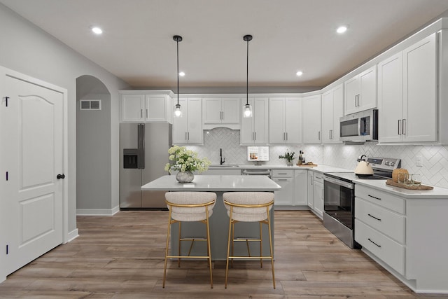 kitchen with decorative light fixtures, stainless steel appliances, a kitchen island, and light hardwood / wood-style flooring