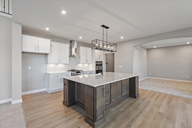 kitchen featuring white cabinetry, a center island with sink, wall chimney range hood, and light hardwood / wood-style flooring