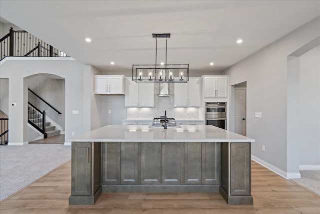 kitchen featuring white cabinetry, a large island, double oven, and light wood-type flooring