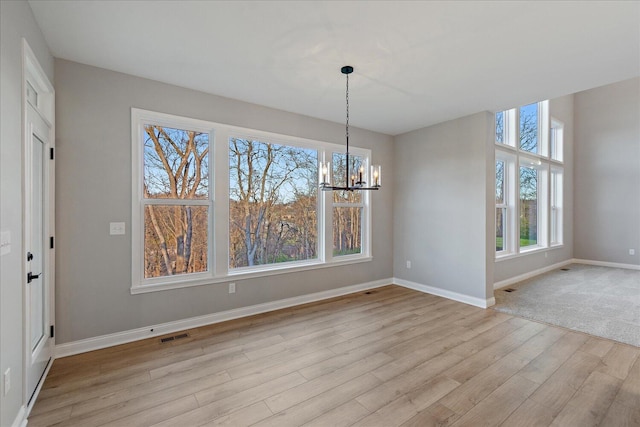 unfurnished dining area featuring light hardwood / wood-style floors, a wealth of natural light, and a chandelier