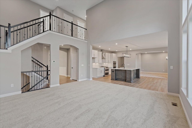 unfurnished living room with a wealth of natural light, light carpet, sink, and a towering ceiling