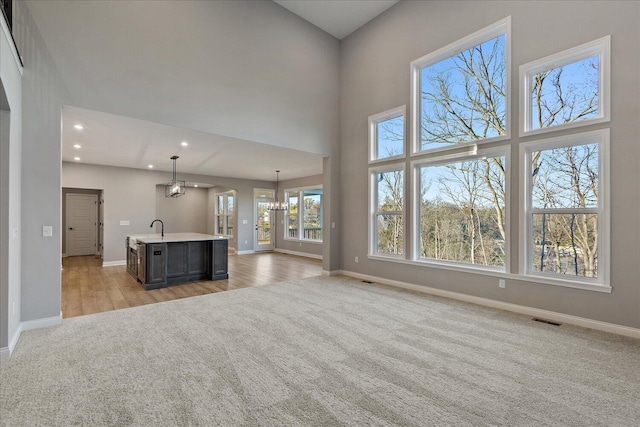 unfurnished living room featuring a notable chandelier, sink, light carpet, and a high ceiling