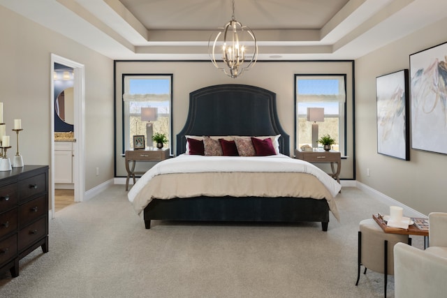 carpeted bedroom featuring ensuite bath, a notable chandelier, and a tray ceiling